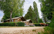 Tienda safari Villatent Wood en Camping Le Coin Tranquille, Francia, rodeada de árboles y una hamaca naranja.