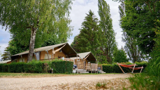 Safaritent Villatent Wood op Camping Le Coin Tranquille in Frankrijk, omringd door bomen en een oranje hangmat.