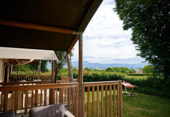Vista dalla terrazza di una tenda safari Villatent Wood presso Camping Le Coin Tranquille, Francia, con natura verde.