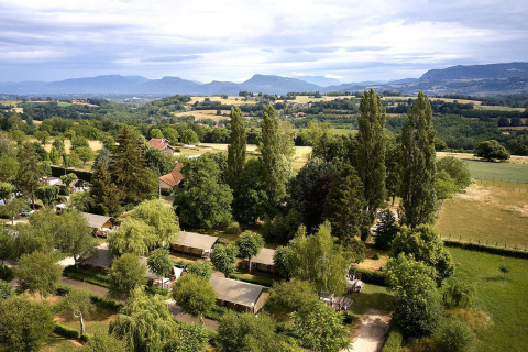 Vista aérea de las tiendas safari Villatent Wood en Camping Le Coin Tranquille en Francia con montañas al fondo.