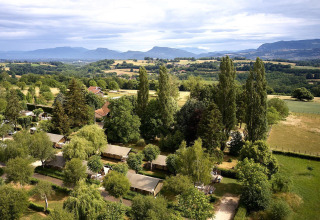 Vista aerea delle tende safari Villatent Wood al Camping Le Coin Tranquille in Francia con le montagne sullo sfondo.