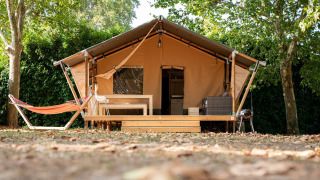 Tienda safari Villatent Nomad con terraza de madera y hamaca en Camping La Garenne en Francia, rodeada de árboles.