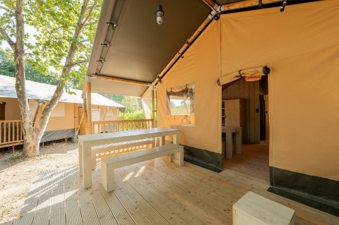 Terraza de tienda safari con bancos de madera en Villatent Nomad, Camping La Garenne, Francia.