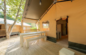 Terraza de tienda safari con bancos de madera en Villatent Nomad, Camping La Garenne, Francia.