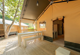 Terraza de tienda safari con bancos de madera en Villatent Nomad, Camping La Garenne, Francia.