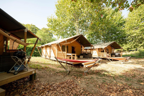 Tiendas safari Villatent Nomad en Camping La Garenne, Francia, rodeadas de árboles y con terrazas de descanso.