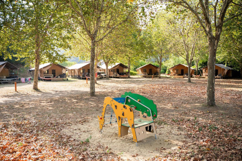 Tiendas safari Villatent Nomad en Camping La Garenne en Francia, rodeadas de árboles y un parque infantil.