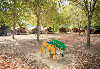 Tiendas safari Villatent Nomad en Camping La Garenne en Francia, rodeadas de árboles y un parque infantil.