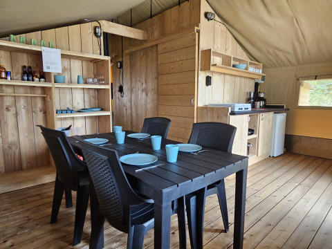 Intérieur d'une tente Safari avec sanitaires, table à manger, coin cuisine et mobilier en bois.