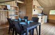 Interno di tenda Safari con servizi igienici, tavolo da pranzo, cucina e arredamento in legno.