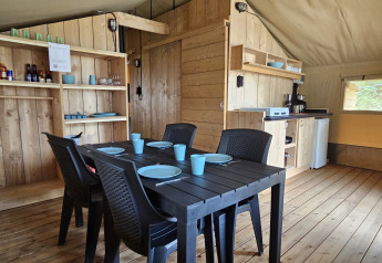 Interior of a Safari tent with sanitary facilities, dining table, kitchen area, and wooden furnishings.