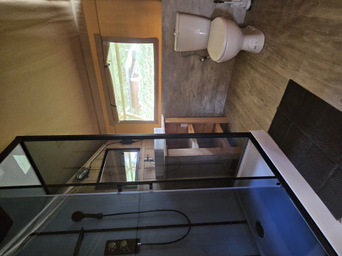 Salle de bain dans une tente safari au lodge avec douche, toilettes, fenêtre et meubles en bois.