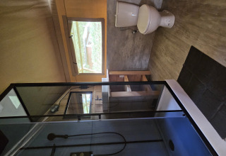 Bathroom of a safari tent lodge featuring a shower, toilet, window and wooden furniture.