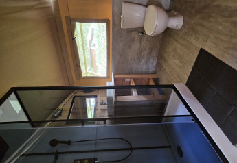 Salle de bain dans une tente safari au lodge avec douche, toilettes, fenêtre et meubles en bois.