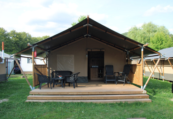 Safari-Zelt mit Veranda und Sitzgelegenheiten auf Camping Vallee de L'Our in Luxemburg, Außenansicht.