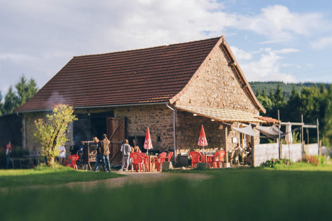 Casa de piedra con techo rojo y sillas en un parque vacacional en Auvergne-Rhône-Alpes, Francia