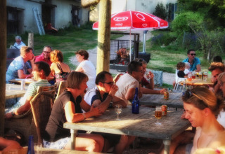 Folk nyder en solrig eftermiddag på Camping Domaine La Chabanne med drinks og samtaler udendørs.