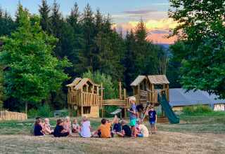 Børn leger på en legeplads omgivet af træer i Camping Domaine La Chabanne, Auvergne-Rhône-Alpes, Frankrig.