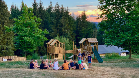 Kinder spielen auf einem Spielplatz im Camping Domaine La Chabanne, umgeben von Bäumen in Auvergne-Rhône-Alpes.