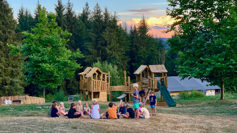Children play on a wooden playground at Camping Domaine La Chabanne, surrounded by trees in rural France.