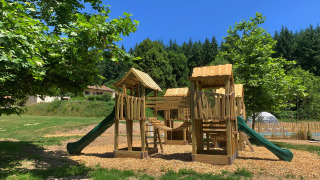 Parque infantil de madera con toboganes y estructuras para trepar en Camping Domaine La Chabanne, Francia.