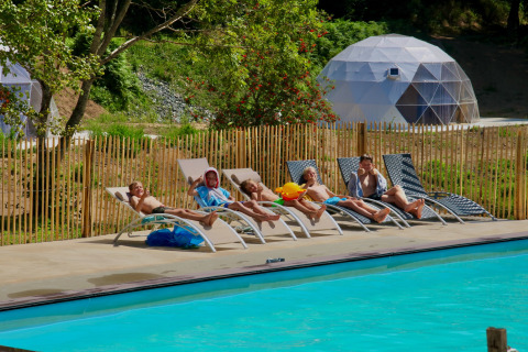 Niños relajándose en tumbonas junto a la piscina con tiendas domo geodésicas al fondo en un parque vacacional.