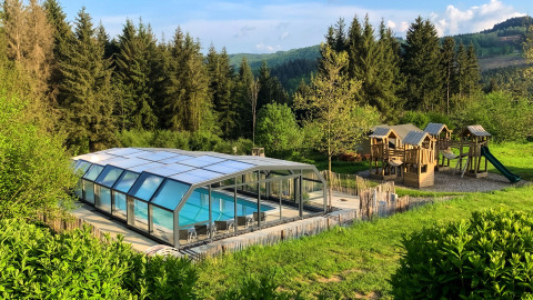 Piscina cubierta y parque infantil de madera en Dome, Camping Domaine La Chabanne, rodeados de bosque en Francia.