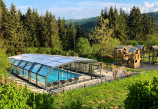 Piscina cubierta y parque infantil de madera en Dome, Camping Domaine La Chabanne, rodeados de bosque en Francia.