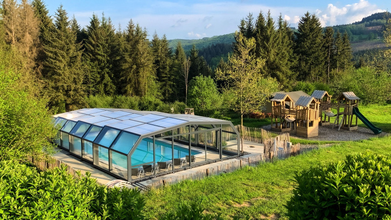 Piscine couverte et aire de jeux au Dome du Camping Domaine La Chabanne, entourées de forêt verdoyante en France.