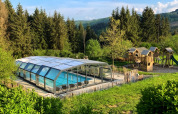 Covered pool and wooden playground at Dome, Camping Domaine La Chabanne, set in lush greenery and forest in France.