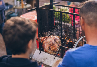 Two people grilling meat over an open fire at Camping Domaine La Chabanne in Auvergne-Rhône-Alpes, France.
