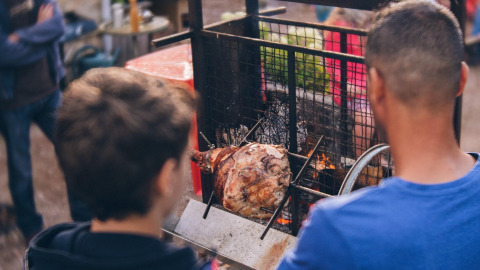 Two people grilling meat over an open fire at Camping Domaine La Chabanne in Auvergne-Rhône-Alpes, France.