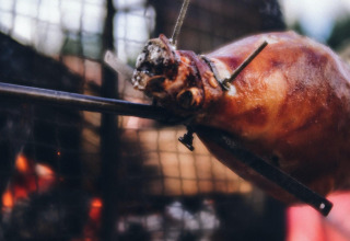 Primo piano di un agnello intero arrosto allo spiedo su fuoco al Camping Domaine La Chabanne, Auvergne-Rhône-Alpes, Francia.