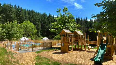 Parco giochi e piscina all'aperto circondati da alberi al Camping Domaine La Chabanne in Auvergne-Rhône-Alpes.