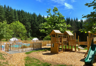 Parco giochi e piscina all'aperto circondati da alberi al Camping Domaine La Chabanne in Auvergne-Rhône-Alpes.