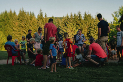 Famiglie e bambini radunati attorno a un falò presso il Camping Domaine La Chabanne, Auvergne-Rhône-Alpes, Francia.