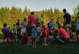 Famiglie e bambini radunati attorno a un falò presso il Camping Domaine La Chabanne, Auvergne-Rhône-Alpes, Francia.