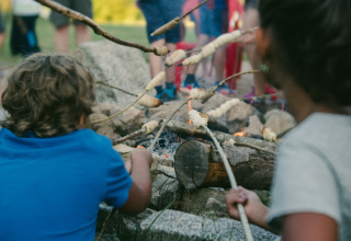 Bambini che arrostiscono pane su bastoncini attorno al fuoco a Camping Domaine La Chabanne in Alvernia, Francia.