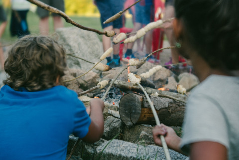 Bambini che arrostiscono pane su bastoncini attorno al fuoco a Camping Domaine La Chabanne in Alvernia, Francia.