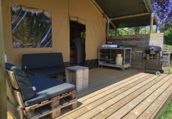 Veranda in legno di una tenda safari con mobili in pallet, cucina esterna e barbecue a gas.