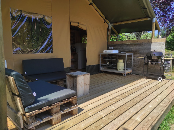 Terrasse en bois devant tente safari avec meubles en palettes, cuisine extérieure et barbecue à gaz.