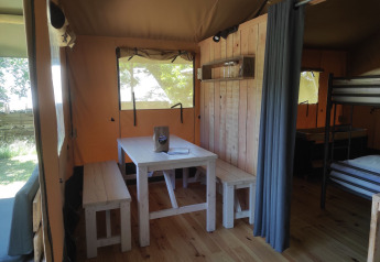 Vista interna di una tenda safari con tavolo in legno, panche, letto a castello e pareti in legno.