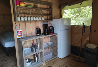 Cozy kitchenette inside a safari tent featuring wooden shelves, fridge, coffee makers, and tableware.