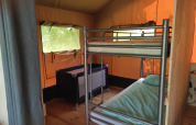 Interno di una tenda safari con letto a castello, lettino, pavimento in legno e finestre luminose.