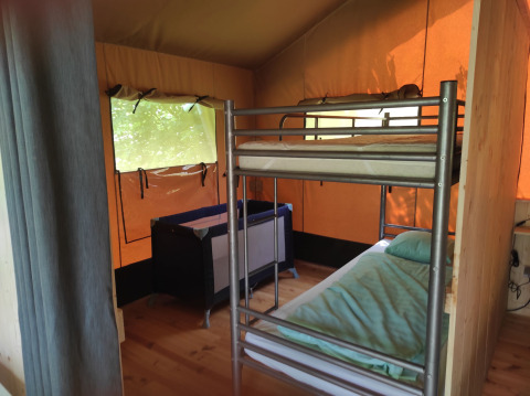 Interno di una tenda safari con letto a castello, lettino, pavimento in legno e finestre luminose.