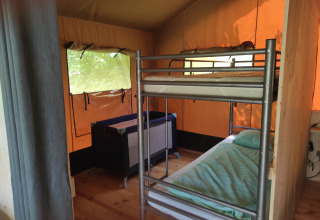 Interno di una tenda safari con letto a castello, lettino, pavimento in legno e finestre luminose.