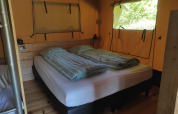 Vista interna di una tenda safari con letto matrimoniale, lenzuola a righe e finestre sulla natura.