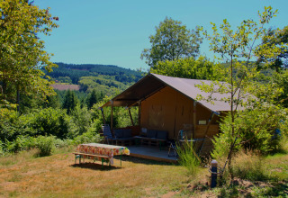 Tienda safari Greenlodge en el Camping Domaine La Chabanne en Francia, rodeada de naturaleza y montañas verdes.