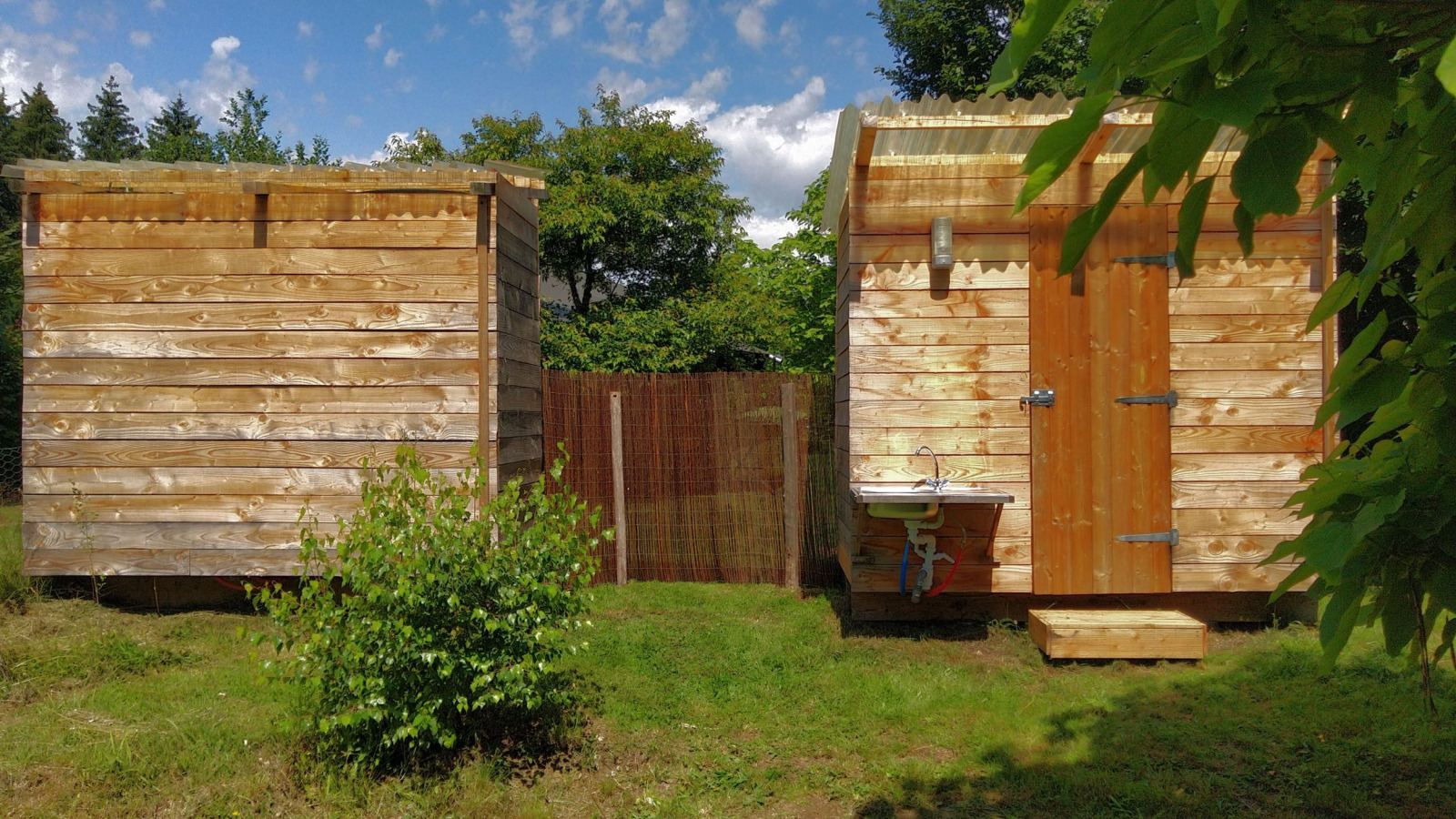 Twee houten hutten en een buitenwastafel bij Safari Greenlodge, Camping Domaine La Chabanne, Frankrijk.