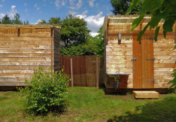 Twee houten cabines en een buitenwastafel bij Safari Greenlodge, Camping Domaine La Chabanne, Frankrijk.